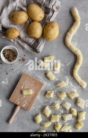 De dessus vue de dessus de dessus de gnocchi non cuit avec pomme de terre et poivre placé près du couteau et de la planche striée sur la table grise pendant la préparation du déjeuner dans la cuisine Banque D'Images