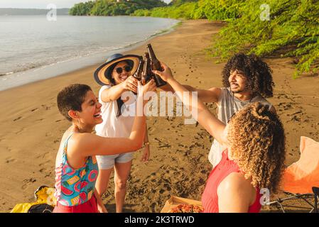 De haut groupe de jeunes amis heureux de griller avec des bouteilles de bière tout en se rassemblant sur la plage de sable en été au Costa Rica Banque D'Images