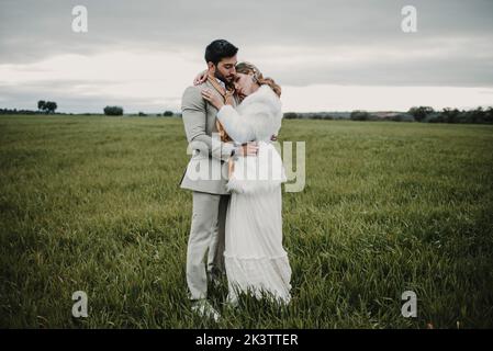 Vue latérale d'un jeune garçon en costume avec une dame en robe de mariage et un manteau sur fond flou Banque D'Images