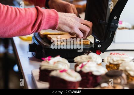 Vue latérale de la récolte anonyme cuisinier préparer de savoureux sandwiches vegan dans la presse panini placé sur la table dans le bakehouse Banque D'Images