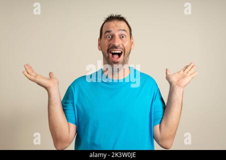 Drôle homme souriant dans un t-shirt bleu montrant les paumes vers le haut, geste surprise inattendu isolé sur fond beige. Beau heureux homme qui entend de bonnes nouvelles Banque D'Images