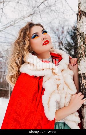 Une fille en vêtements rouges s'appuie sur une neige d'hiver de bouleau Banque D'Images