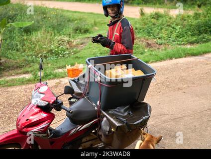 Un service de messagerie de moto livre des colis dans une zone rurale. Banque D'Images