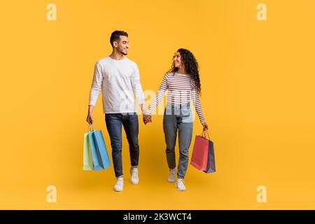 Ventes importantes. Joyeux couple arabe marchant avec des sacs de shopping sur fond jaune Banque D'Images