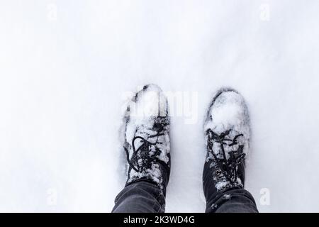 pieds dans des bottes noires sur un sol enneigé. L'arrivée de l'hiver et du temps enneigé. Banque D'Images