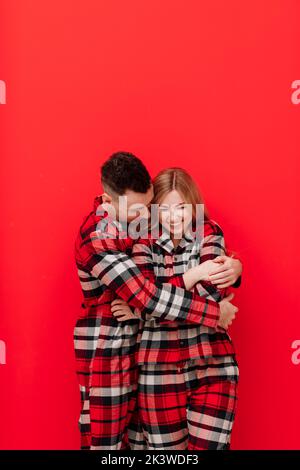 Bonne Saint Valentin. Jeune couple dans le même pyjama est embrassant et embrassant sur fond rouge.l'homme et la femme dans l'amour aiment dépenser tim Banque D'Images