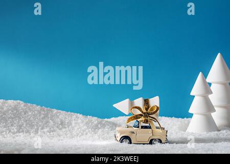 Une petite voiture jouet transportant un arbre de Noël au milieu d'une forêt enneigée Banque D'Images