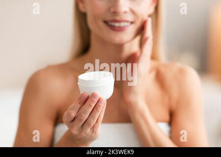 Concept de soins de la peau. Femme d'âge moyen méconnaissable tenant un pot de crème hydratante, mise au point sélective, écourtée Banque D'Images