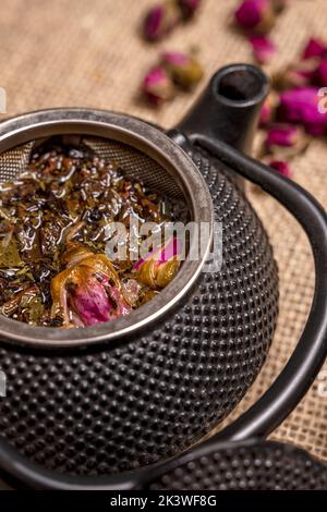 Vue rapprochée d'une théière en métal noir de style asiatique avec thé rose et thé vert dans le panier Banque D'Images