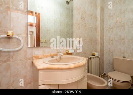 Salle de bains avec armoires blanches, miroir sans cadre sur le mur et dessus en marbre rose veiné Banque D'Images