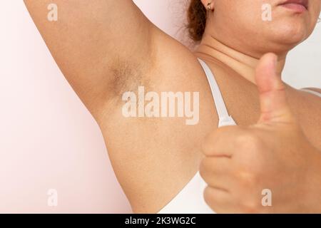 Gros plan sur une aisselle non rasée. Cheveux sur les mains de la femme. Concept de positivité du corps, auto-acceptation. La main donne les pouces vers le haut Banque D'Images