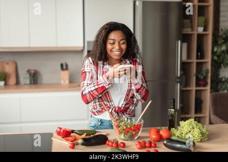 Joyeuse femme afro-américaine millénaire faire une photo de salade avec des légumes biologiques, profiter de repas de cuisine Banque D'Images