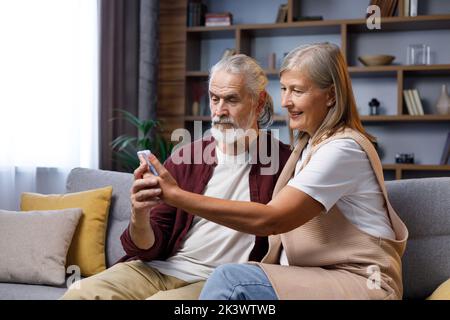 Un couple heureux mûr communique un appel en ligne. Un mari et une femme aux cheveux gris parlent à des parents au téléphone. Appel vidéo sur smartphone. À distance Banque D'Images