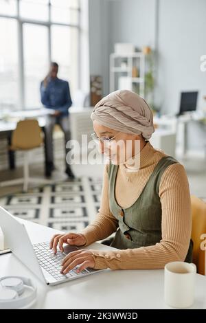 Portrait vertical d'une jeune femme d'affaires du Moyen-Orient portant un serre-tête au bureau et dactylographiant sur un ordinateur portable Banque D'Images