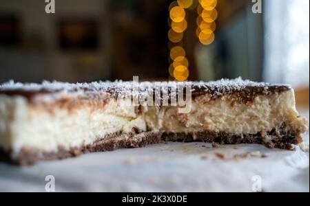 Gâteau de Bounty fait maison avec lait de coco et crème au chocolat sur une assiette blanche avec une cuillère contre la lumière de bokeh Banque D'Images