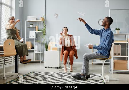 Une équipe diversifiée de jeunes professionnels s'amusant au bureau et prenant des avions de papier, de la communication et des idées concept Banque D'Images