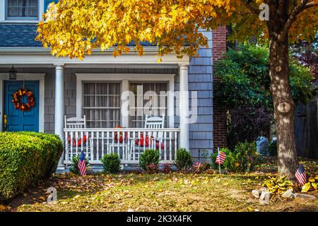 Entrée bleue à deux maisons de stockage avec porche et fauteuils à bascule et drapeaux américains et une couronne d'automne sous un érable d'automne à feuilles jaunes - cl Banque D'Images