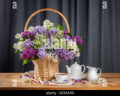 bouquet de lilas dans un panier sur la table. tasse de thé, théière et pot à lait. concept thé d'été Banque D'Images