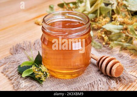 Un pot de miel, un bâton de miel et des fleurs de tilleul sur une vieille planche. Concept rustique Banque D'Images