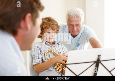 Transmettre sa sagesse musicale. Un grand-père enseignant à son petit-fils comment jouer la trompette pendant que son père regarde. Banque D'Images