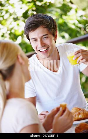 Apportez le petit déjeuner. Un jeune couple heureux prenant le petit déjeuner ensemble sur le patio à la maison. Banque D'Images