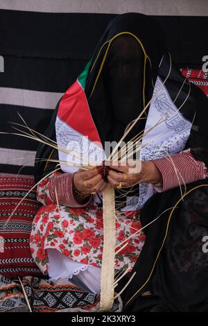 Femme arabe masquée d'Abu Dhabi portant une bande de fabrication d'Abaya à partir de Date palmier Fibre pour une utilisation dans la fabrication des paniers de paille traditionnels. Banque D'Images