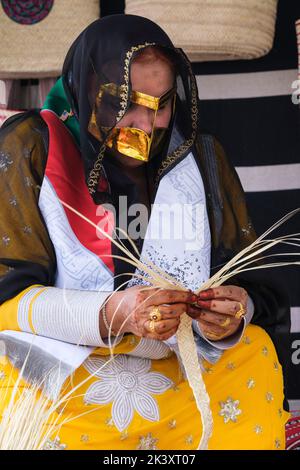 Femme arabe masquée d'Abu Dhabi portant une bande de fabrication d'Abaya à partir de Date palmier Fibre pour une utilisation dans la fabrication des paniers de paille traditionnels. Banque D'Images