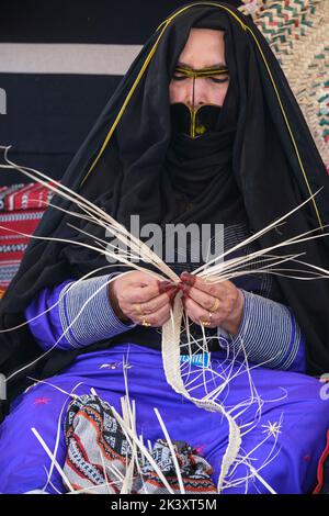 Femme arabe masquée d'Abu Dhabi portant une bande de fabrication d'Abaya à partir de Date palmier Fibre pour une utilisation dans la fabrication des paniers de paille traditionnels. Banque D'Images