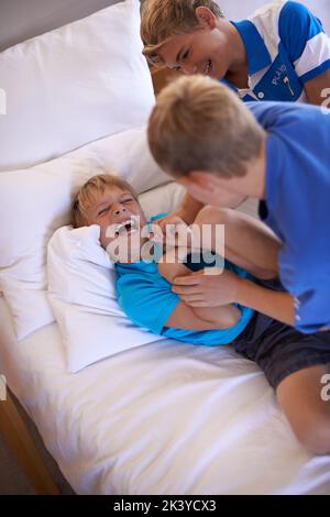 Amuse-toi bien. Un petit garçon joue à la lutte avec ses frères sur le lit. Banque D'Images