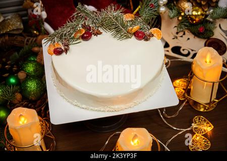 Gâteau de mousse de Noël au goût de l'ananas et aux fruits sur fond de bougies, guirlandes, branches de sapin et cônes Banque D'Images