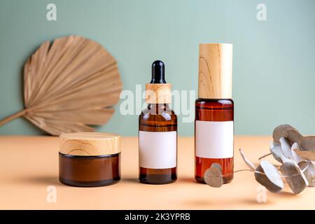 Bouteilles et bocaux de cosmétiques en verre ambré avec couvercles pamboo avec branche d'eucalyptus sèche et feuille de palmier sèche sur fond beige. Produits de beauté automnaux Banque D'Images