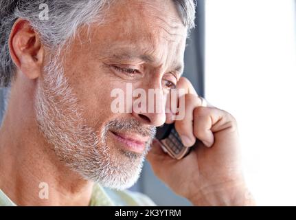 Une conversation téléphonique conviviale. Un homme mûr regardant vers le bas et souriant tout en ayant une conversation téléphonique. Banque D'Images