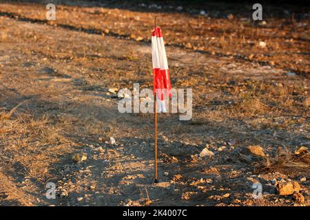 Ruban d'avertissement de danger rouge et blanc brillant neuf rayé attaché sur le dessus du fil de construction en métal rouillé épais à gauche comme signe d'avertissement sur le côté Banque D'Images