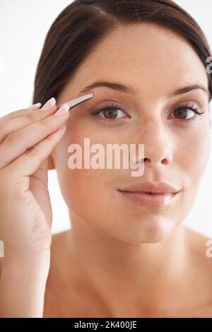 Façonnage avec précaution. Portrait d'une jeune femme attirante qui plendit ses sourcils. Banque D'Images