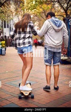 Un jeune homme qui apprend à sa petite amie à faire du skateboard. Banque D'Images