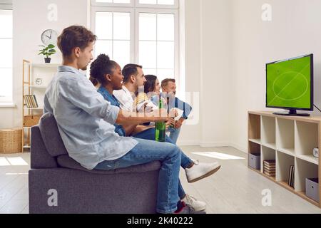 Amis jeunes garçons et filles regardent un match de football à la télévision ensemble assis sur un canapé. Banque D'Images