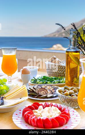 Petit déjeuner d'été frais maison avec jus d'orange, tomates cerises, fromage, olives, concombre, œufs une tasse de café sur le balcon avec vue sur la mer. CA Banque D'Images