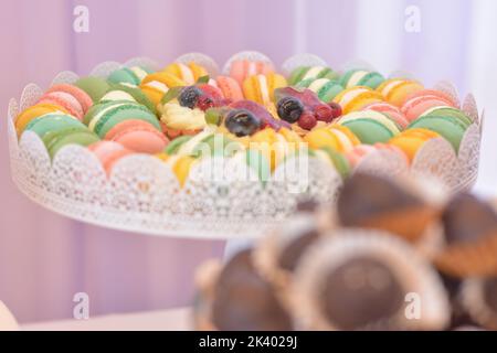 Plateau avec macarons colorés et mini-tartes avec fruits et crème vanille au milieu Banque D'Images