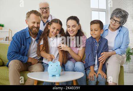 Une grande famille positive jette des pièces de monnaie dans la banque de piggy collectant de l'argent pour la voiture, le voyage et l'éducation. Banque D'Images