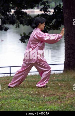 ILLUSION OPTIQUE. Une femme faisant du tai Chi dans une robe rose semble pousser un arbre qui est en fait plus loin. Dans un parc à Queens, New York. Banque D'Images