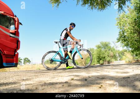 Cycliste s'est arrêté sur son vélo de course sur la route avec tout son équipement de sécurité: Casque, lunettes de soleil, sécurité. Avec un camion passant Banque D'Images