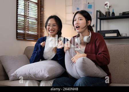 Deux jeunes femmes qui applaudissent ensemble pour le sport à la télévision dans un salon confortable à la maison Banque D'Images