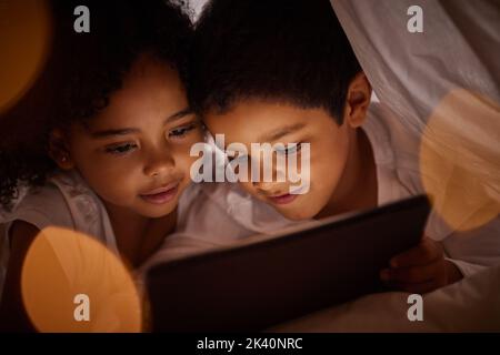 Enfants, tablette numérique et films en streaming sur Internet dans une couverture amusante fort à la maison la nuit. Heureux, garçon et fille enfants jouant et appréciant en ligne Banque D'Images