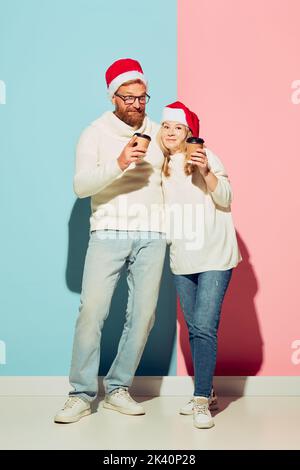 Jeune couple charmant portant des chapeaux de noël et des chandails chauds blancs goûtant du café. Concept romantique. Banque D'Images