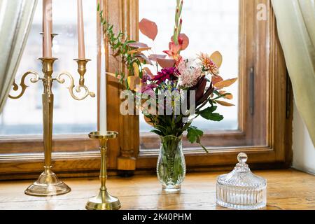 Deux bougies allumées dans un chandelier en bronze un vieux livre ouvert et un bouquet de fleurs colorées sur le rebord de la fenêtre à côté de la fenêtre dans la soirée Banque D'Images