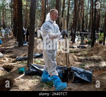 19 septembre 2022, Izyum, Ukraine: Un investigateur portant un équipement de protection est vu portant des pelles utilisées pour exhumer les corps. Un site de sépulture de masse a été trouvé dans la périphérie de la ville ukrainienne orientale, Izyum, région de Kharkiv, qui a été libérée de l'occupation russe il y a deux semaines. Au moins 445 nouvelles tombes ont été trouvées sur le site d'un cimetière existant alors que beaucoup n'ont que des numéros écrits sur la croix en bois. Tous les corps seront exhumés et envoyés pour examen médico-légal mais il a été dit lors des premières enquêtes que certains organes ont montré des signes de torture. (Image de crédit : © Ashley Chan/SOPA IM Banque D'Images