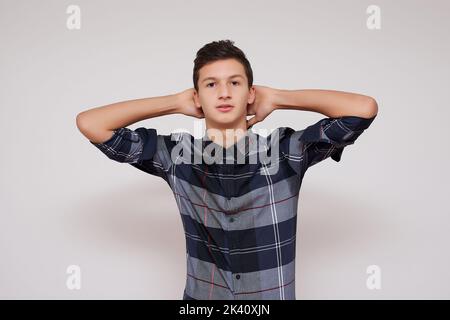 Portrait d'un jeune homme souriant aux cheveux sombres, tenant les mains derrière sa tête sur fond blanc. Banque D'Images