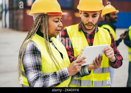 Travailleurs multiraciaux contrôlant les conteneurs d'expédition dans le port industriel extérieur - Focus sur la femme senior africaine visage Banque D'Images