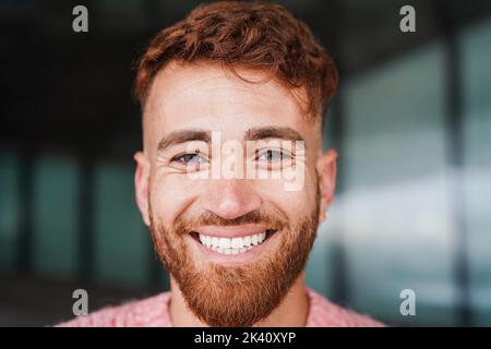 Jeune homme de cheveux rouge souriant sur l'appareil photo extérieur Banque D'Images