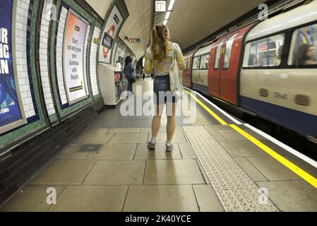 Londres, Angleterre, Royaume-Uni. Jeune femme en short denim sur une plate-forme de station de métro. Tooting Broadway. Banque D'Images